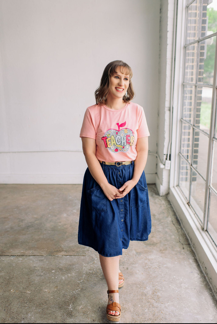 Sleep Training Pricing & Packages In Fort Worth Smiling sleep consultant wearing a pink t-shirt and blue skirt stands confidently, ready to help parents with sleep training their 6 month old baby through gentle, personalized support.